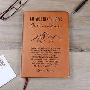 May include: A tan leather-like journal featuring a black mountain graphic and the text: FOR YOUR NEXT CHAPTER Johnathan. Every ending holds the promise of a new beginning. There are still mountains to climb, lessons to learn, and meaningful moments waiting to be lived. As you write your next chapter, step forward with courage and trust the journey ahead. The best is yet to come. Love, Mom.