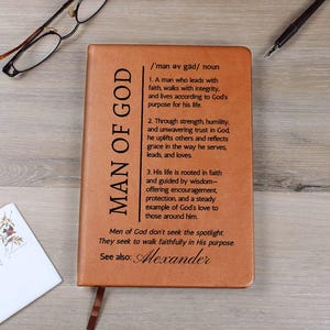 May include: A brown leather journal with the words "MAN OF GOD" printed vertically on the left side. The journal has text describing the qualities of a man of God. A bookmark is attached.