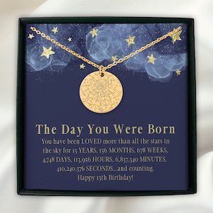 May include: A gold-colored necklace with a round pendant featuring a star map design. The necklace is displayed on a dark blue background with text that reads "The Day You Were Born" and "Happy 13th Birthday!" with star illustrations.