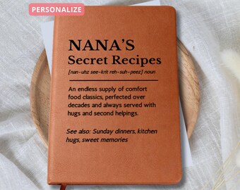 May include: A brown leather-bound notebook with the text "NANA'S Secret Recipes" in black. The notebook includes a definition and additional text about comfort food classics. A pink "PERSONALIZE" sticker is in the top left corner.