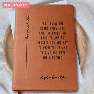 May include: A personalized, brown leather journal with the text "Jeremiah 29:11" and a quote. The quote reads, "For I know the plans I have for you..." and is followed by a name. The journal has a ribbon bookmark.