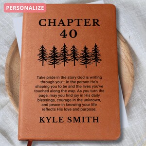 May include: A personalized, brown leather journal with the text "CHAPTER 40" and a row of pine trees. The journal includes an inspirational quote and the name "KYLE SMITH". The word "PERSONALIZE" is in a pink box in the upper left corner.