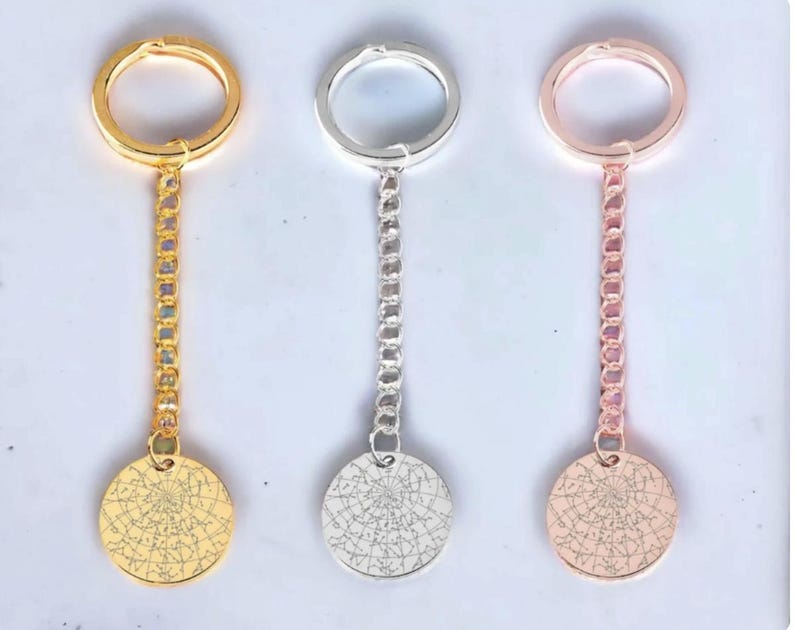 May include: Three keychains with round pendants featuring a star map design. One is gold-colored, one is silver-colored, and the third is rose gold. Each keychain has a chain connecting the pendant to a ring.