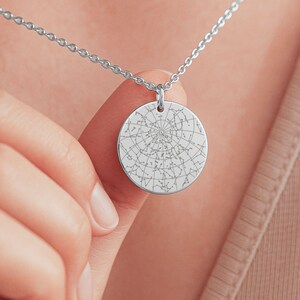 May include: A silver-colored necklace featuring a circular pendant engraved with a detailed star map. The pendant is suspended from a delicate chain. The design showcases a celestial theme, perfect for those interested in astronomy or astrology.