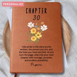 May include: A brown leather journal with the text "CHAPTER 30" and a floral design. The journal includes the text "Take pride in the story you've written..." and the name "Piper". The word "PERSONALIZE" is in a pink box in the upper left corner.