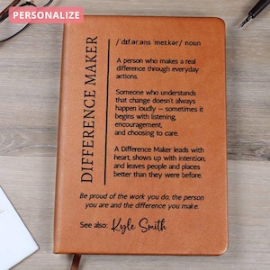 Könnte beinhalten: Ein braunes Lederjournal mit dem Text "DIFFERENCE MAKER" vertikal auf der linken Seite gedruckt. Das Journal enthält eine Definition und inspirierenden Text. Das Wort "PERSONALISIEREN" befindet sich in einem rosa Feld oben links.