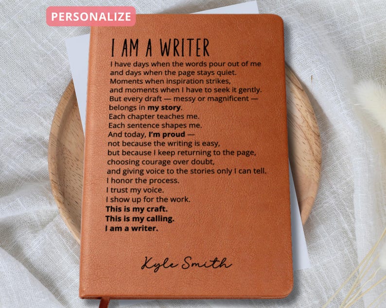 May include: A brown leather journal with the text "I AM A WRITER" and a poem printed on the inside pages. The journal is personalized with the name "Kyle Smith" at the bottom. The word "PERSONALIZE" is in a pink box at the top.