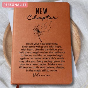 May include: A personalized orange journal with the words "NEW Chapter" and a dandelion illustration. The journal includes inspirational text and the name "Olivia". A red ribbon bookmark is visible.