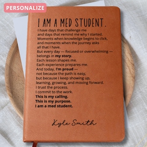 May include: A personalized, brown leather journal with the text "I AM A MED STUDENT." The journal includes an inspirational poem and the name "Kyle Smith" at the bottom. A red ribbon bookmark is visible.