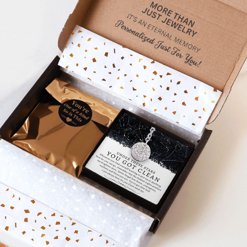 May include: An open gift box with a necklace and a gold-colored pouch. The necklace has a round pendant with a detailed design. The box has text that reads "MORE THAN JUST JEWELRY" and "Personalized Just For You!"