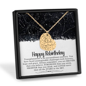 Puede incluir: Un collar con colgante dorado en forma de coraz&oacute;n con un dise&ntilde;o de constelaci&oacute;n, presentado en una caja de regalo negra. La caja contiene una tarjeta con el texto "Happy Rebirthday" y un mensaje inspirador sobre la valent&iacute;a.