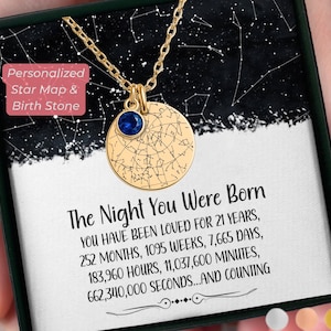 May include: Gold-colored necklace with a round pendant featuring a star map design and a blue gemstone. The necklace is presented in a black box with the text "The Night You Were Born" and other details about time. The box also has the text "Personalized Star Map & Birth Stone".