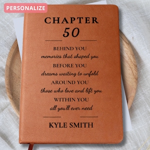 May include: A brown leather journal with the text "CHAPTER 50" and inspirational text. The journal is personalized with the name "KYLE SMITH" at the bottom. A red ribbon bookmark is visible.