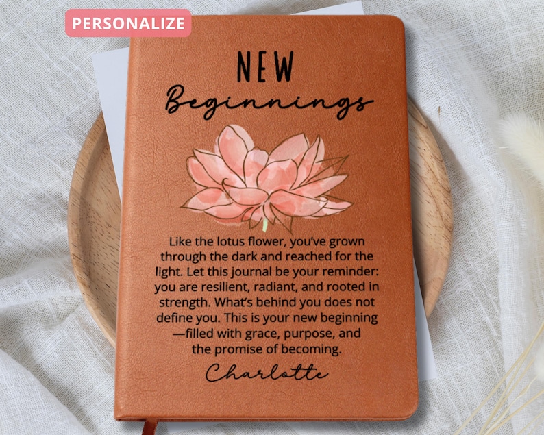 May include: A brown journal with the words "NEW Beginnings" and a lotus flower illustration. The journal has inspirational text and the name "Charlotte". The word "PERSONALIZE" is in a pink box. The journal is designed for personal use.