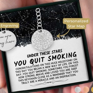 May include: A silver keychain with a star map design and the words "you are my hero" engraved on the back. The keychain is presented in a black gift box with a starry night background and the text "YOU QUIT SMOKING".
