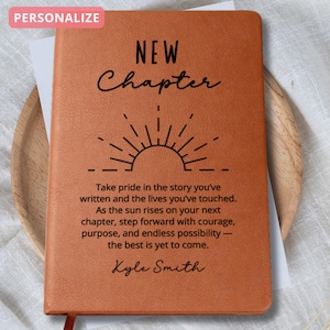 May include: A brown leather journal with the words "NEW Chapter" and a sunburst design. The journal includes the text "Take pride in the story you've written...the best is yet to come." and the name "Kyle Smith".