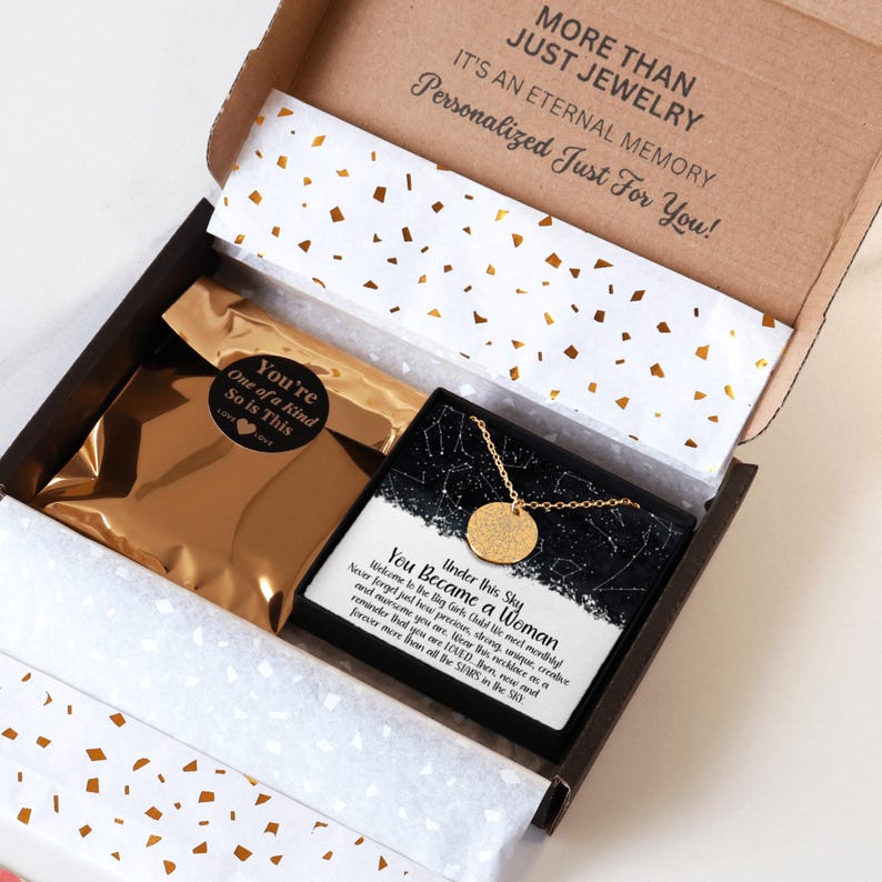 May include: A gift box with a gold necklace and a card that reads "Under this sky you became a woman". The box is open and the necklace is visible. The card has a black and white starry sky design.