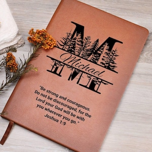 May include: A brown leather journal with a personalized name and a forest scene with a large letter "M" in the center. The quote "Be strong and courageous. Do not be discouraged, for the Lord your God will be with you wherever you go." Joshua 1:9 is engraved on the front.