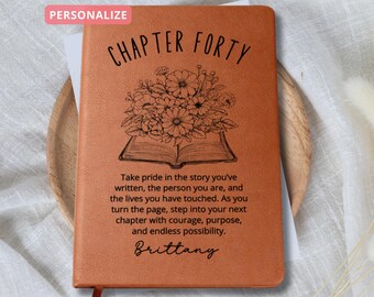 May include: A brown leather journal with the text "CHAPTER FORTY" and a floral design. The journal has the text "Take pride in the story you've written, the person you are, and the lives you have touched. As you turn the page, step into your next chapter with courage, purpose, and endless possibility." and the name "Brittany" written on it.