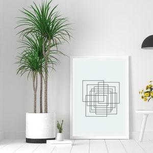 May include: A white framed print with a black and white geometric design of overlapping squares on a light blue background. A potted plant with green leaves is in the foreground.