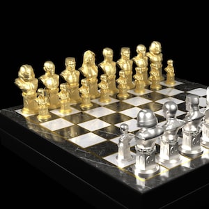 May include: A chess set with gold and silver pieces arranged on a checkered board. The chess pieces are sculpted in the form of busts. The board is set on a black marble base.