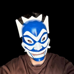 May include: A blue and white mask with a smiling face. The mask has a sharp, angular design and is made of a hard material.