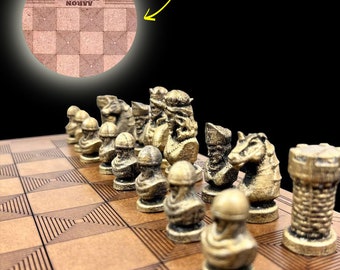 May include: A wooden chess set with bronze-colored chess pieces. The board has a geometric design and the name "AARON SALISBURY" is engraved on the top left corner. The words "PERSONALIZED NAME" are written in yellow.