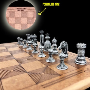 May include: A wooden chessboard with a personalised name, "SALISBURY AARON", engraved on the board. The chess pieces are made of metal and have a silver finish.