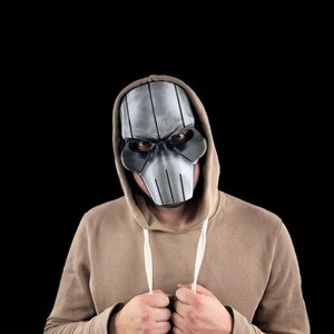 May include: A person wearing a brown hooded sweatshirt with a silver and black skull mask.
