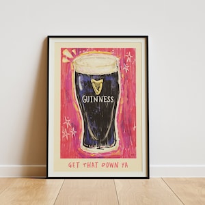 Puede incluir: Un p&oacute;ster enmarcado con fondo rosa y una ilustraci&oacute;n de dibujos animados de un vaso de cerveza Guinness. El texto "GET THAT DOWN YA" est&aacute; en la parte inferior del p&oacute;ster.