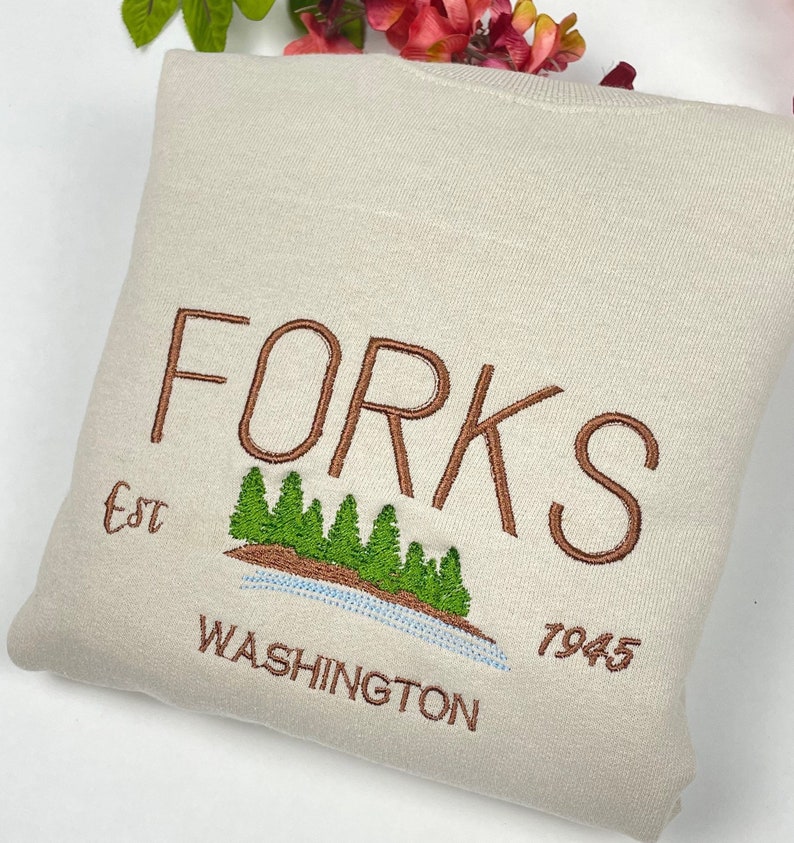 May include: A beige sweatshirt with brown embroidery that reads "FORKS Est. 7945 WASHINGTON" with a green tree graphic.