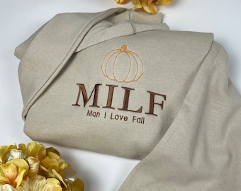May include: A beige sweatshirt with a brown embroidered pumpkin and the text "MILF Man I Love Fall".