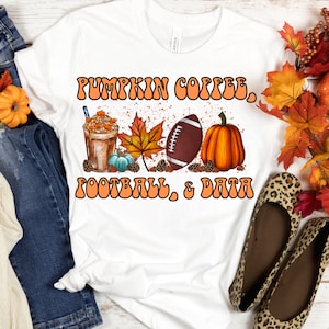 Puede incluir: Camiseta blanca con un diseño gráfico de un latte de calabaza, un balón de fútbol y una calabaza con el texto "Pumpkin Coffee, Football, & Data" en letras naranjas.
