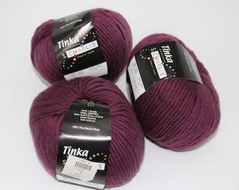 May include: Three skeins of deep burgundy yarn, labeled "Tinka S. Charles," made of 100% fine merino wool. The yarn is tightly wound, with labels displaying product information. Ideal for knitting or crocheting projects.