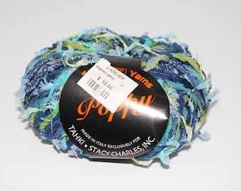 May include: A ball of Poppy Spool yarn in shades of blue, green, and yellow. The yarn has a textured, fringed appearance. A black label with the text "Poppy" and "Tahki Stacy Charles, Inc." is attached.