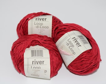 May include: Three balls of red yarn with white labels. The labels read "river Loop -d-Loop" and include a barcode. The yarn is a vibrant red color, and the texture appears soft and slightly textured. The yarn is made of 90% cotton and 10% cashmere.