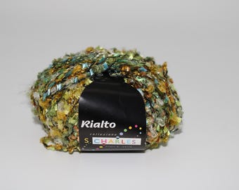 May include: A ball of Rialto brand yarn in a mix of green, gold, and blue colors. The yarn has a textured, ribbon-like appearance. A black label with white text is wrapped around the yarn.