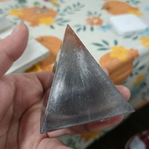 May include: A silver pyramid-shaped object with a smooth, reflective surface.