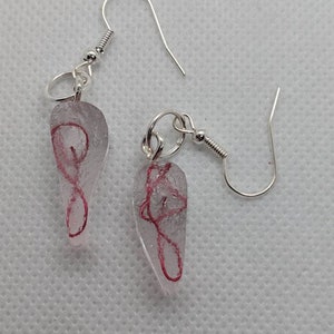 May include: A pair of silver earrings with clear teardrop-shaped glass pendants. The glass is filled with a delicate pink swirl.