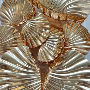 Puede incluir: Primer plano de varias pinzas para el pelo doradas. Cada pinza tiene un diseño en forma de abanico con múltiples crestas curvas. Las pinzas están dispuestas en un grupo, reflejando la luz y creando una apariencia brillante. Accesorios para el cabello.