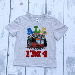 May include: A gray t-shirt with a colorful "All Aboard I'm 4" graphic featuring a cartoon train.