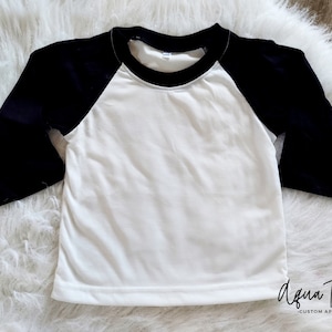 May include: White baseball tee with black sleeves. The shirt has a black ribbed crew neck.