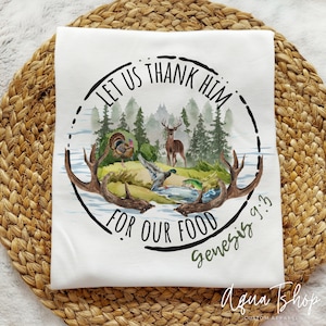 May include: White t-shirt with a black circle design featuring a watercolor illustration of a forest scene with a deer, a turkey, and a duck. The text "LET US THANK HIM FOR OUR FOOD Genesis 9:3" is written around the circle.