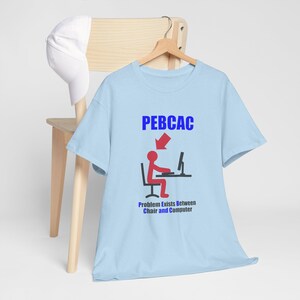 May include: Light blue t-shirt with the text "PEBCAC" in blue, a red arrow, and a stick figure at a computer. Below, the text reads "Problem Exists Between Chair and Computer."