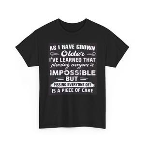 May include: Black t-shirt with white text. The text reads: "AS I HAVE GROWN Older I'VE LEARNED THAT pleasing everyone is IMPOSSIBLE = BUT = PISSING EVERYONE OFF IS A PIECE OF CAKE."