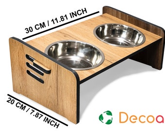 May include: A wooden pet food stand with two stainless steel bowls. The stand is 11.81 inches wide and 7.87 inches tall. The stand has a wood grain finish and black trim. The stand is made by Decoart.