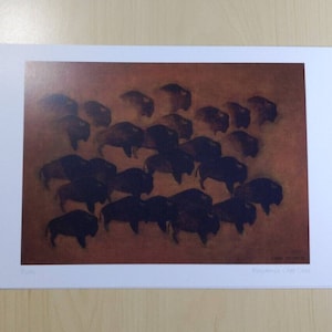 May include: A print featuring a herd of bison in a sepia-toned landscape. The bison are depicted in dark brown silhouettes, creating a sense of movement and depth against the warm background. The print is mounted on a white border.