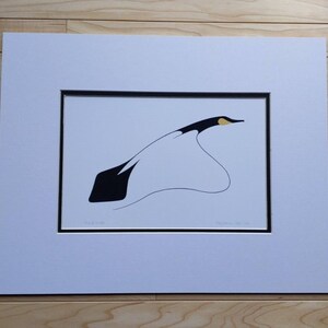 May include: A framed art print featuring a minimalist illustration of a bird in flight. The artwork uses black, white, and yellow colors. The bird's body is black, with a white wing and a yellow beak. The print is matted and framed.