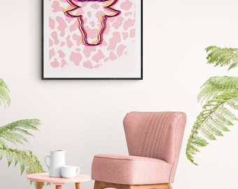 May include: A pink armchair with a wooden frame sits in front of a framed print of a pink and white cow head on a white wall. A pink side table with a white pitcher and cup sits in front of the chair. A pink rug is on the floor.
