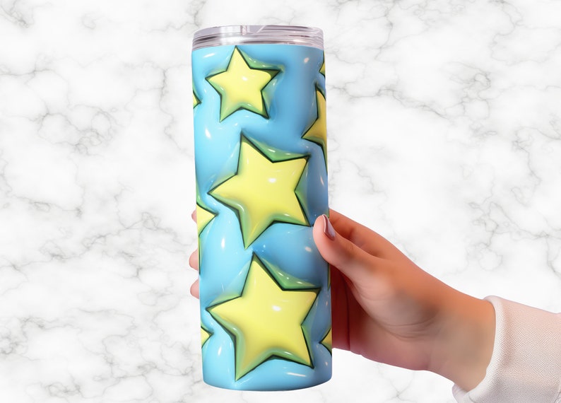 May include: A stainless steel tumbler with a light blue background and yellow stars. The stars have a 3D effect. The tumbler is cylindrical and has a clear lid. The tumbler is held by a person's hand.